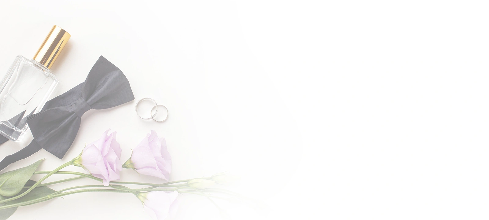Flat Lay von Hochzeitsartikeln, darunter eine
                                    schwarze Fliege, zwei silberne Eheringe, eine
                                    Parfümflasche und hellviolette Blumen auf einem
                                    weißen Hintergrund.